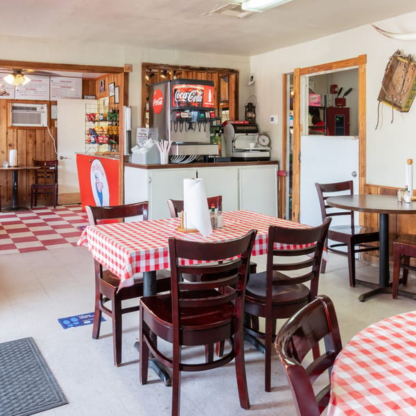 Interior of a casual restaurant with red and white checkered tablecloths and a Coca-Cola soda fountain.