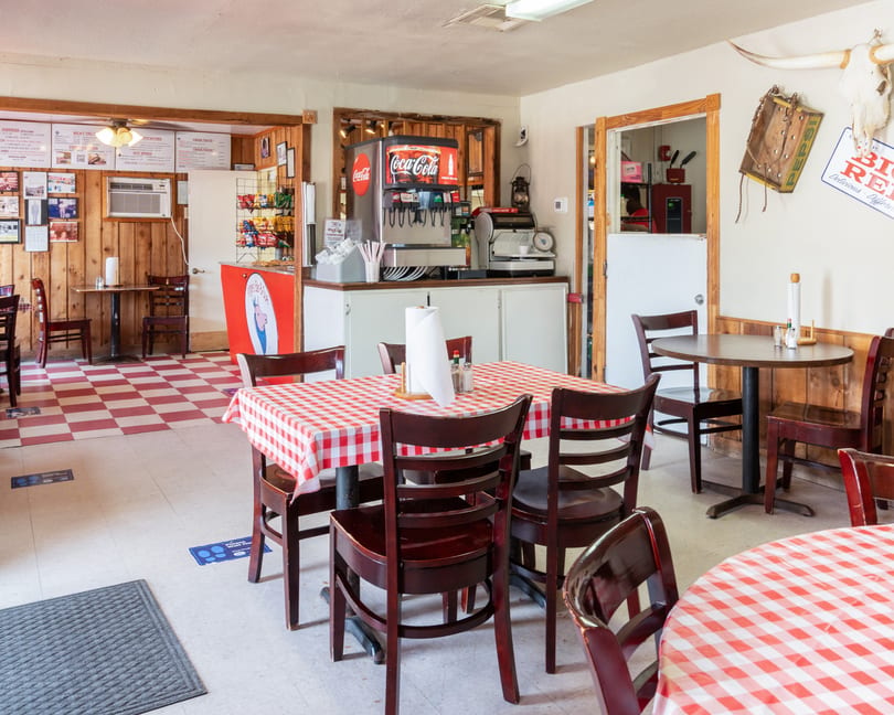 Interior of a casual restaurant with red and white checkered tablecloths and a Coca-Cola soda fountain.