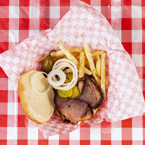 Top-down view of a brisket sandwich with fries, onions, pickles, and a jalapeño on a red and white checkered tablecloth.