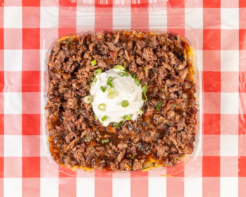 Overhead view of a brisket-topped baked potato with sour cream and green onions on a red and white checkered tablecloth.