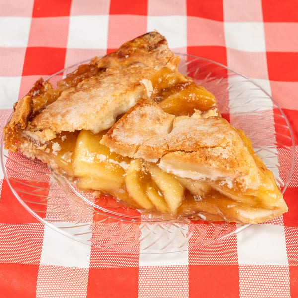 A slice of apple pie with a flaky crust and visible apple filling on a clear plate.