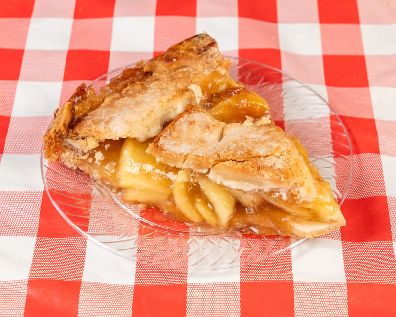 A slice of apple pie with a flaky crust and visible apple filling on a clear plate.