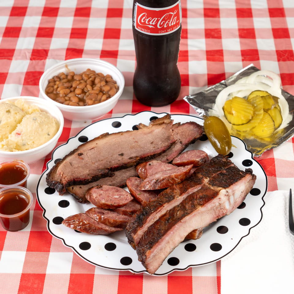 Barbecue platter with brisket, sausage, ribs, baked beans, potato salad, pickles, onions, and a Coke.