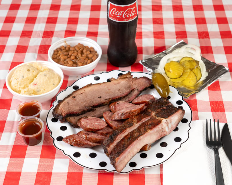 Barbecue platter with brisket, sausage, ribs, baked beans, potato salad, pickles, onions, and a Coke.