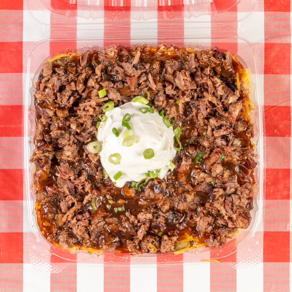 Overhead view of a brisket baked potato with sour cream and green onions on a red and white checkered tablecloth.