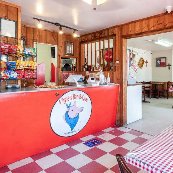 The interior of Virgie's Bar-B-Que features a red counter with a pig logo, snack racks, and dining tables.
