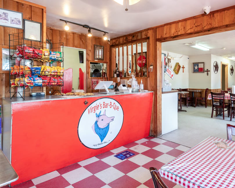 The interior of Virgie's Bar-B-Que features a red counter with a pig logo, snack racks, and dining tables.