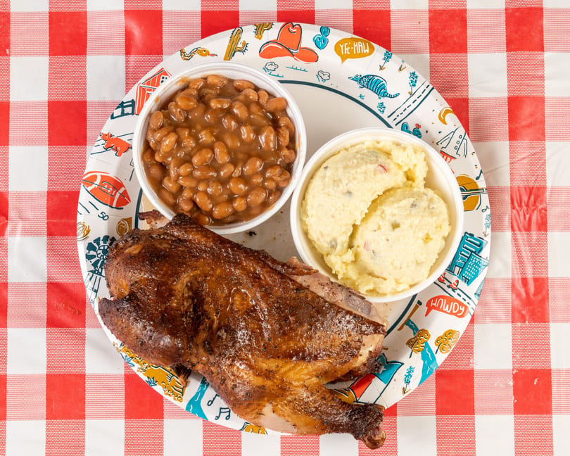 A barbecued chicken half, baked beans, and potato salad on a festive paper plate.