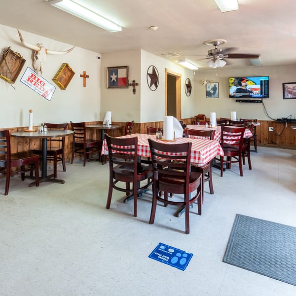A casual restaurant dining room with wooden tables, red and white checkered tablecloths, and Texas-themed decor.