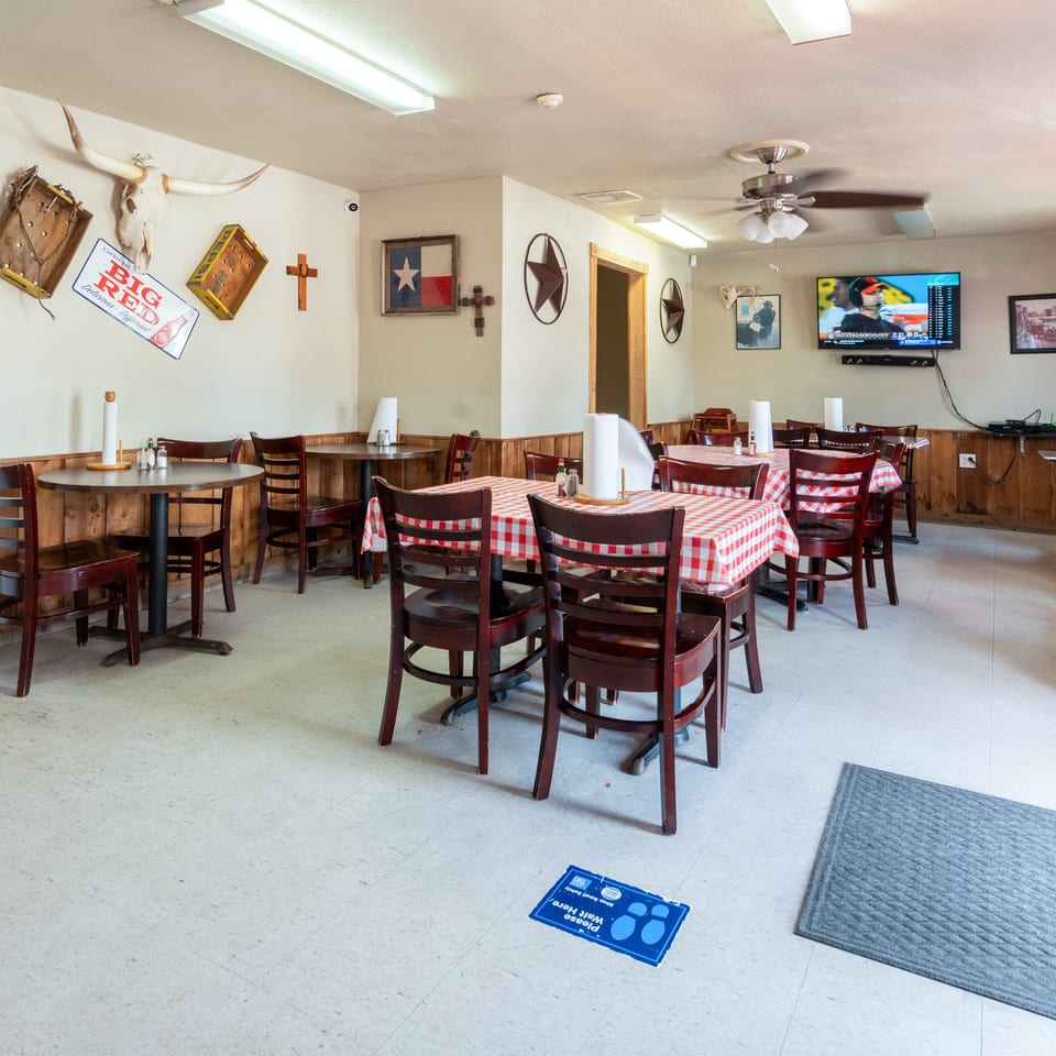 A casual restaurant dining room with wooden tables, red and white checkered tablecloths, and Texas-themed decor.