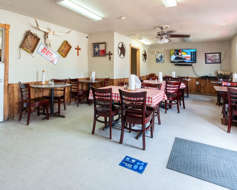 A casual restaurant dining room with wooden tables, red and white checkered tablecloths, and Texas-themed decor.